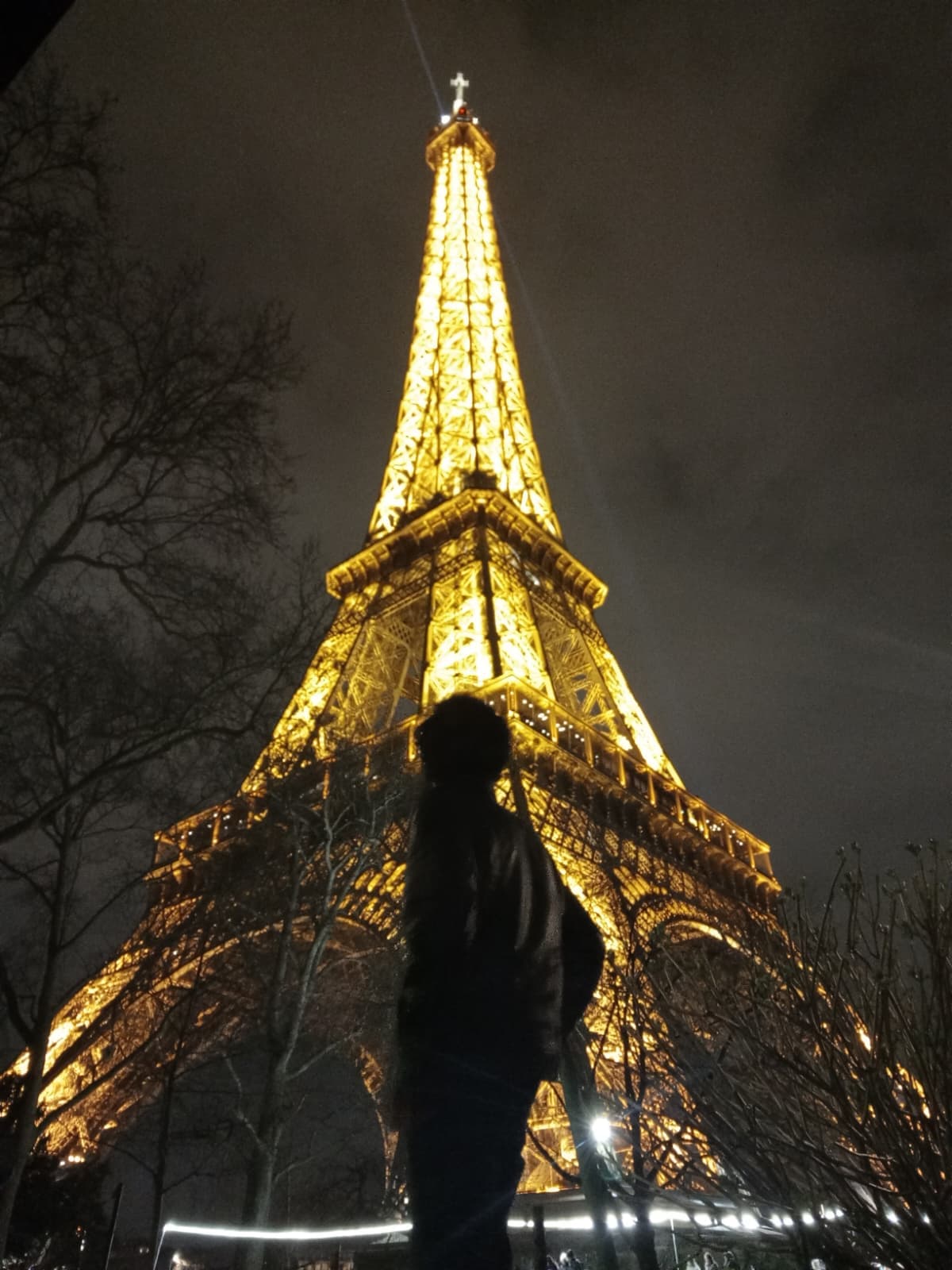 Looking up at the Eiffel Tower glowing at night.