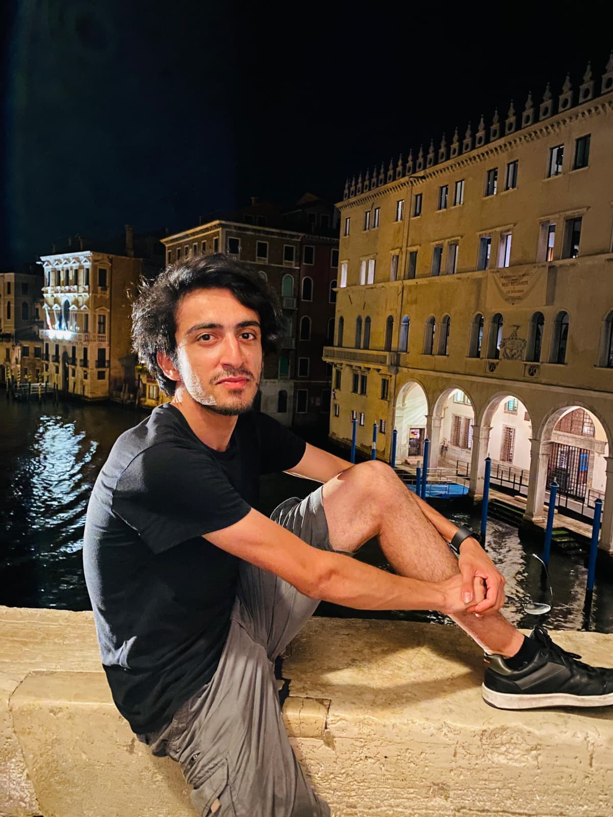 Sitting on a bridge at night with Venice’s canals glowing in the background.