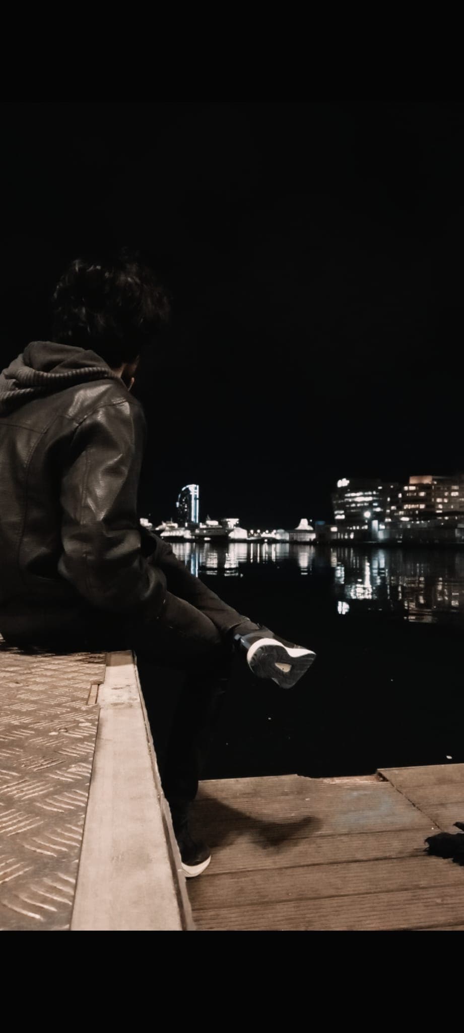 Sitting by the harbor at night, gazing at the lights reflecting on the water.